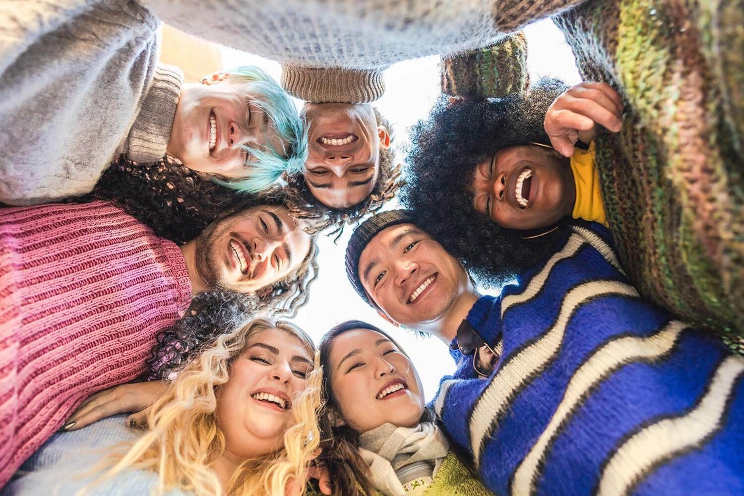 Eine bunte Gruppe junger Freunde umarmt sich fröhlich im Kreis, alle lächeln in die Kamera. Multiethnische Gruppe von Freunden, die gemeinsam Spaß haben.